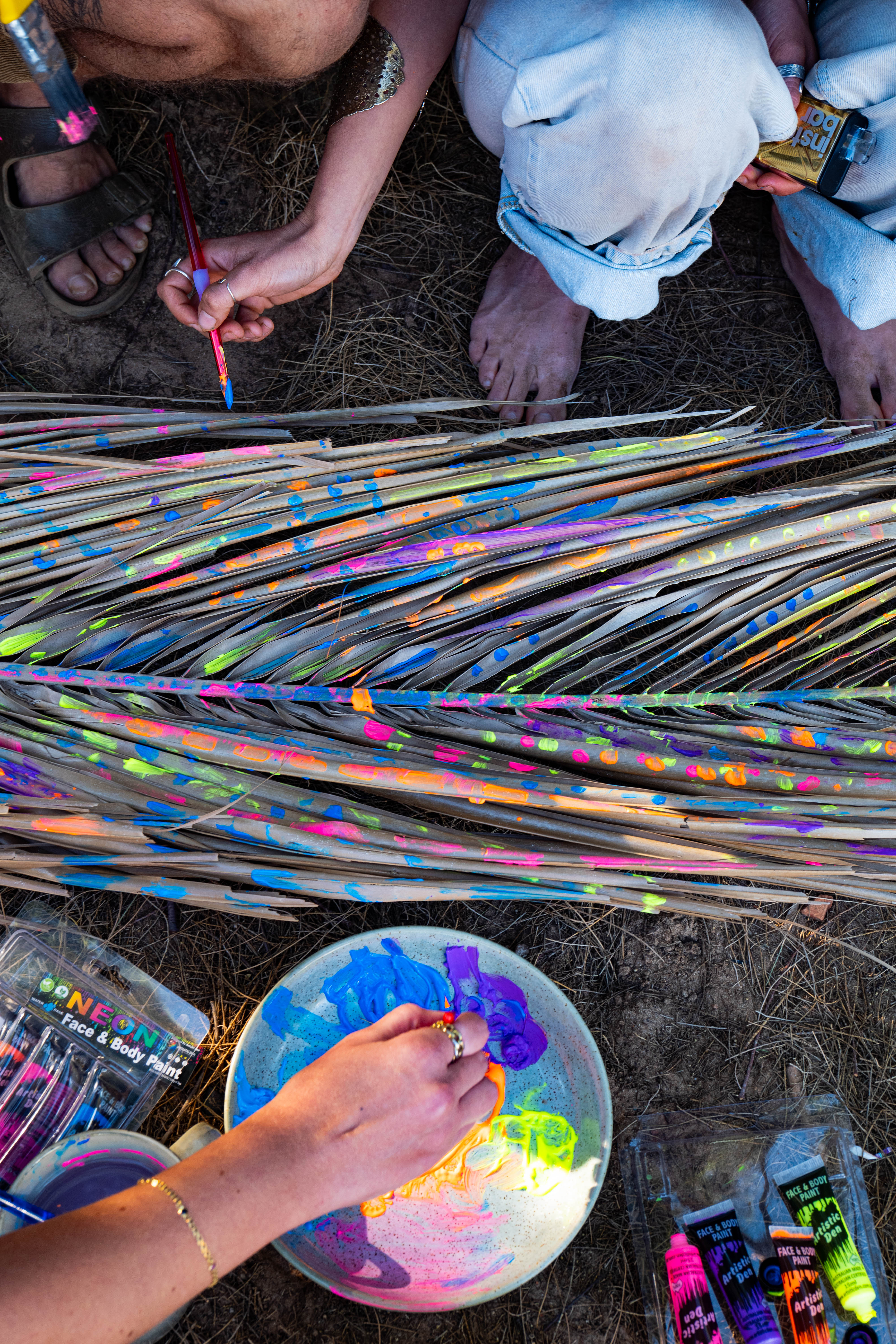 Artists painting dried palm fronds with vivid neon colours