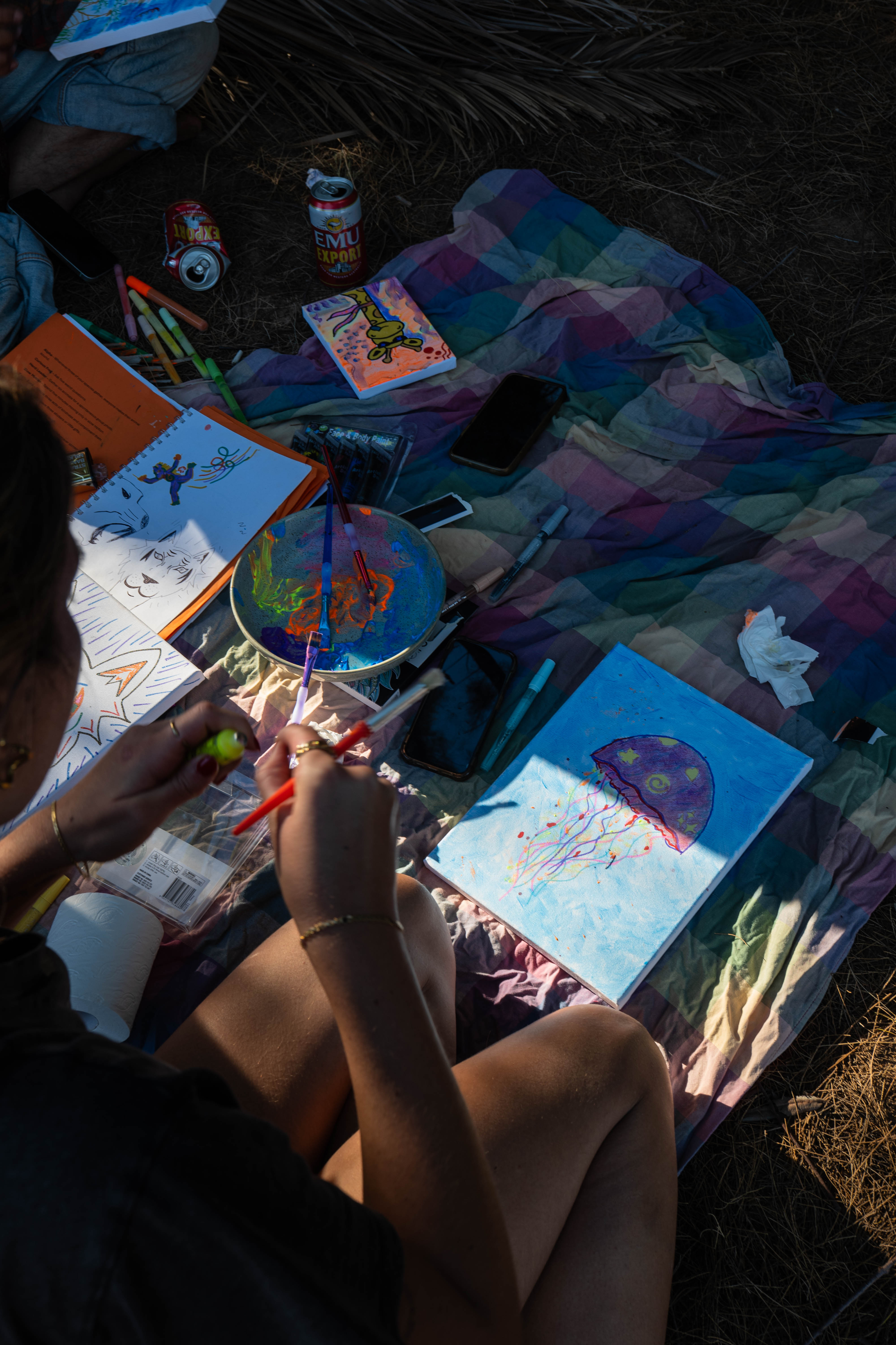 Artists painting colourful canvases together on a picnic blanket