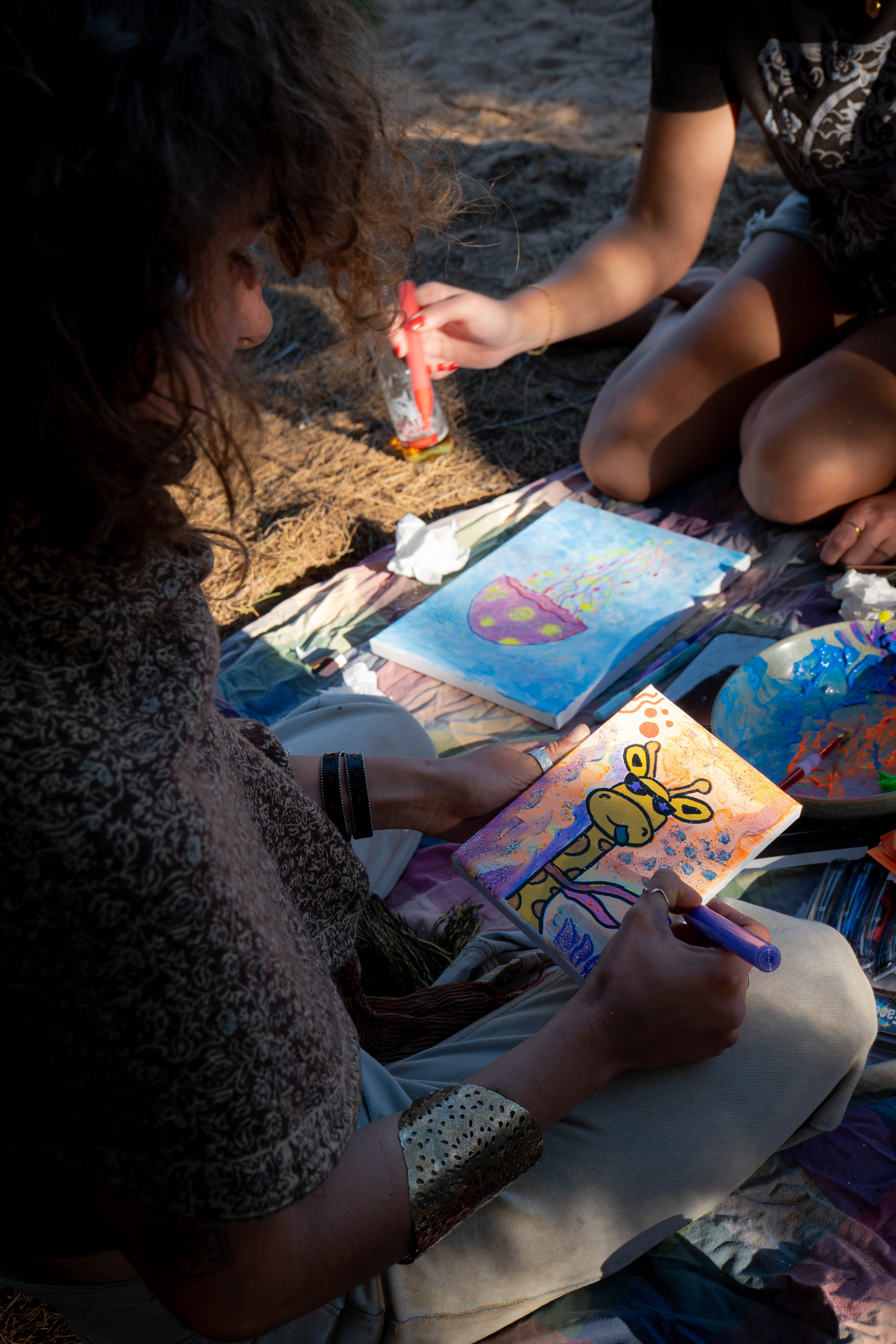 Artists adding colourful details to small canvases at an outdoor gathering