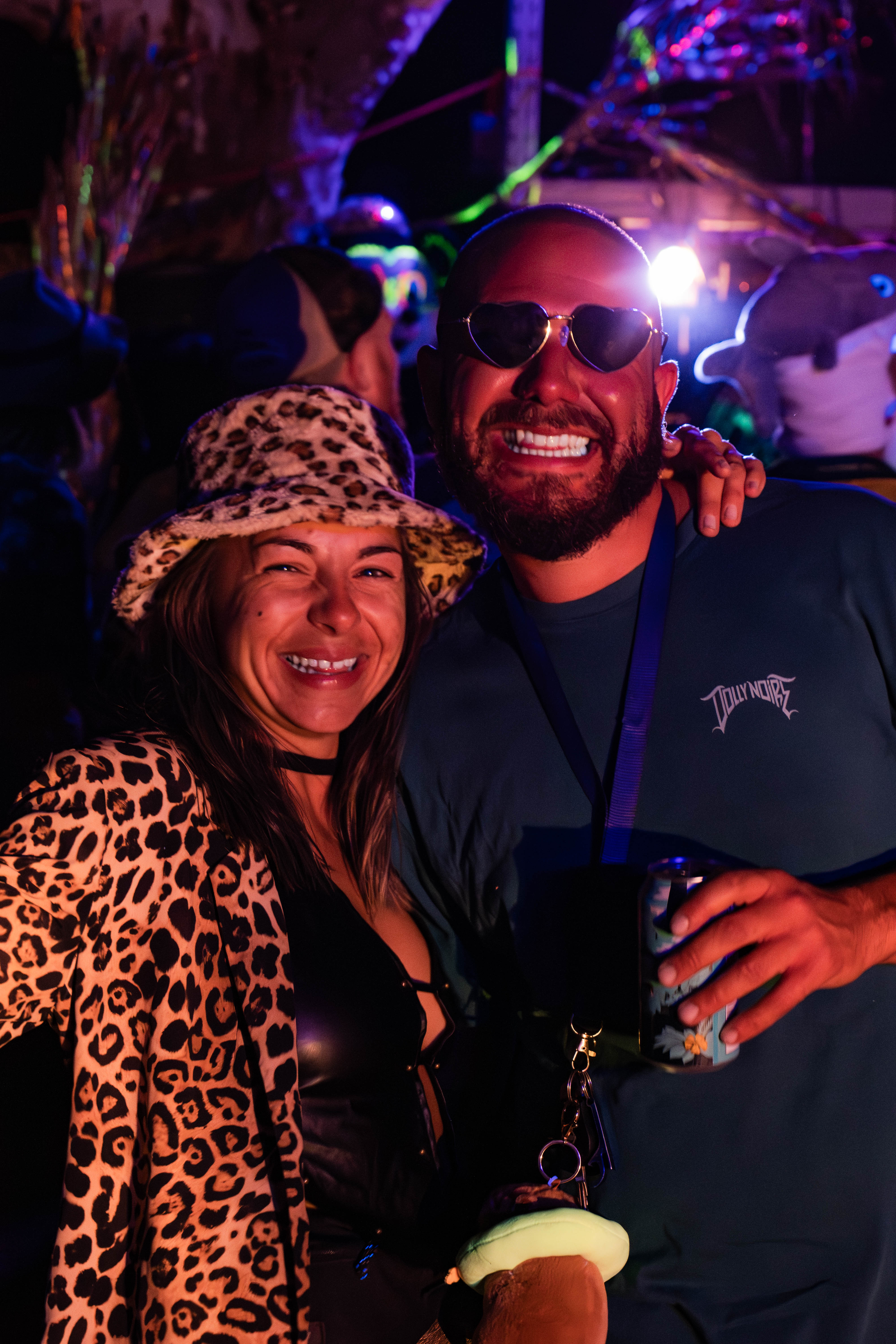 Two festivalgoers smiling together beneath vivid purple and red lights