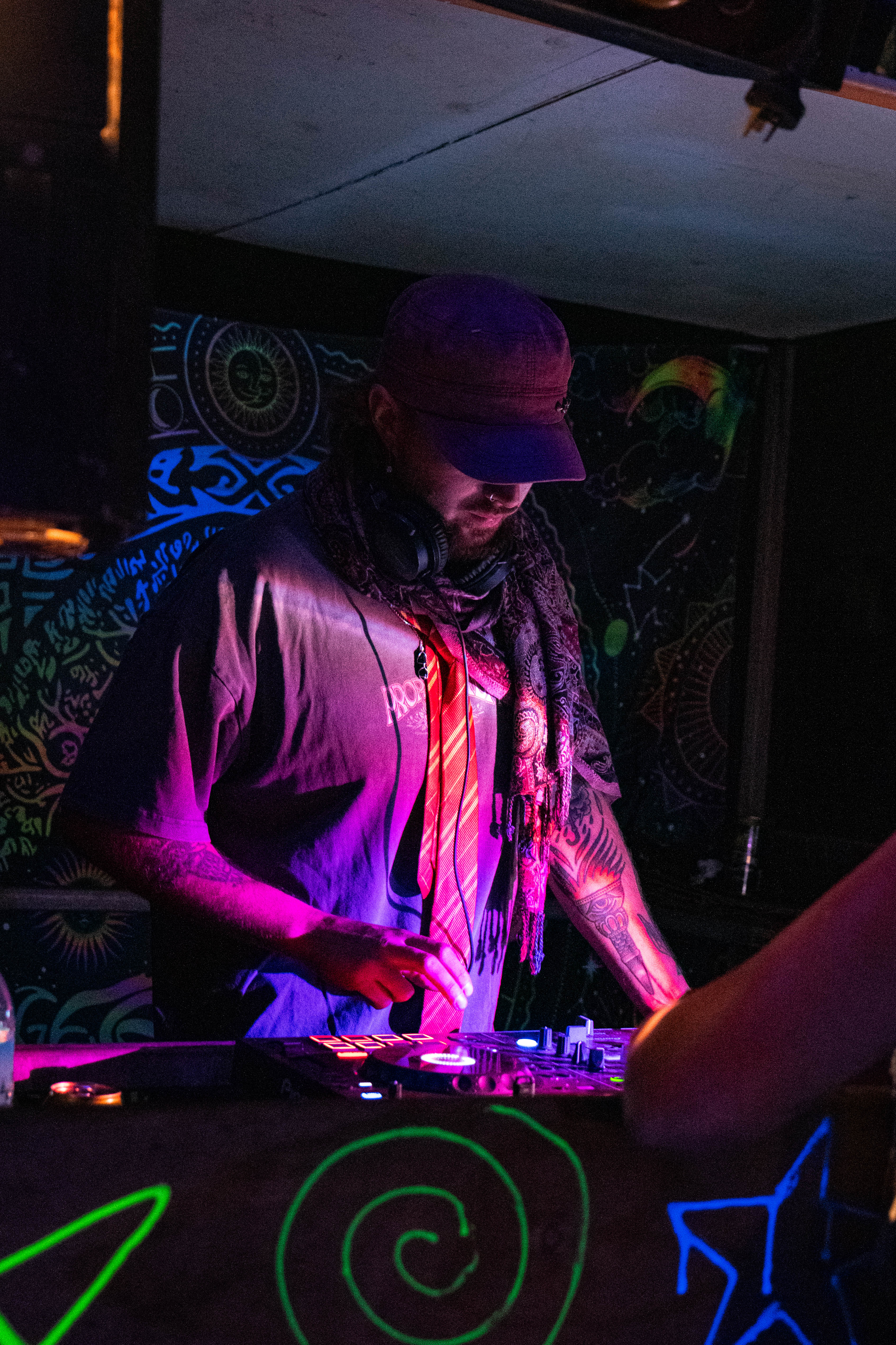A tattooed DJ working at a mixing desk under magenta light