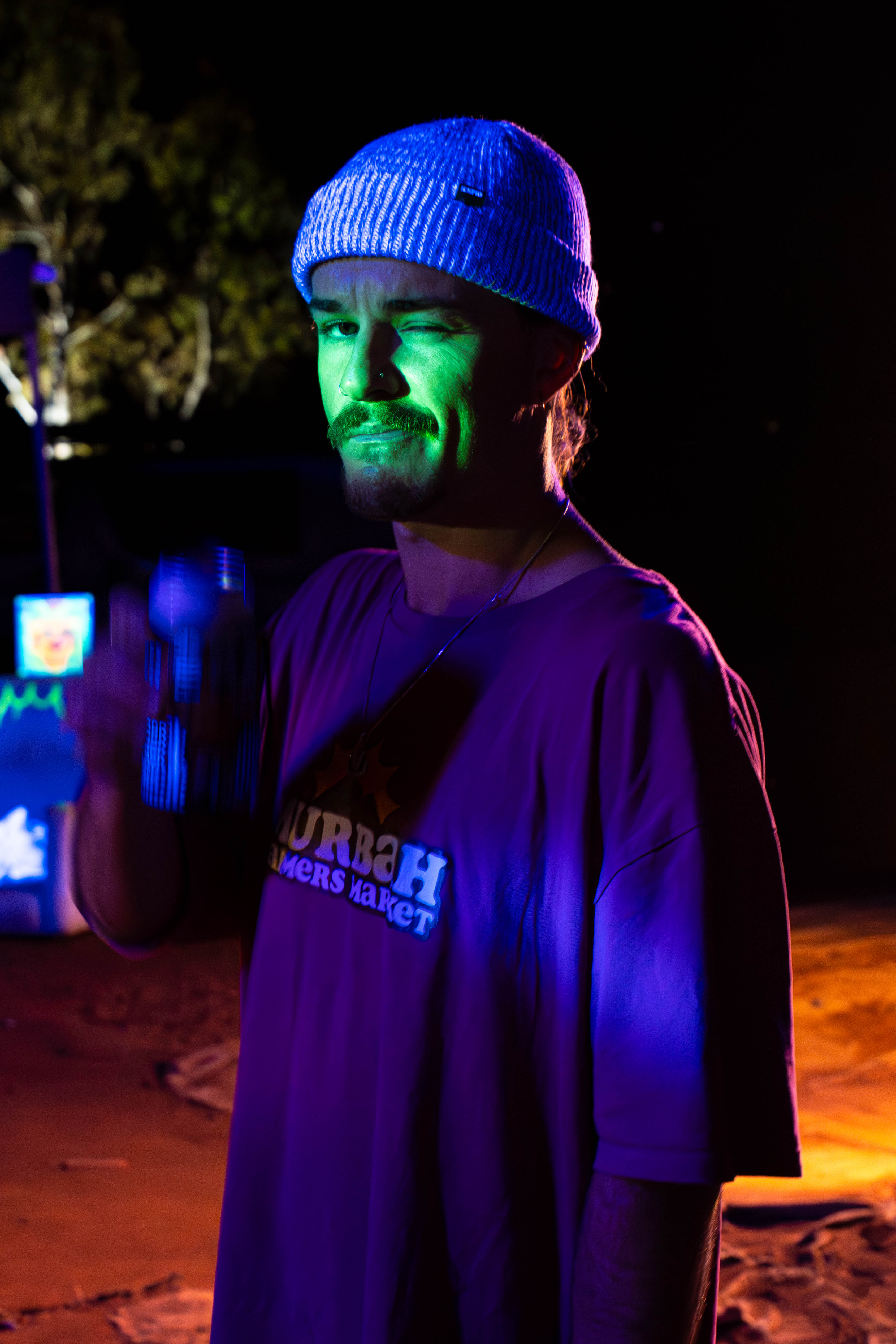 A festivalgoer in a knitted beanie winking beneath blue and green lights