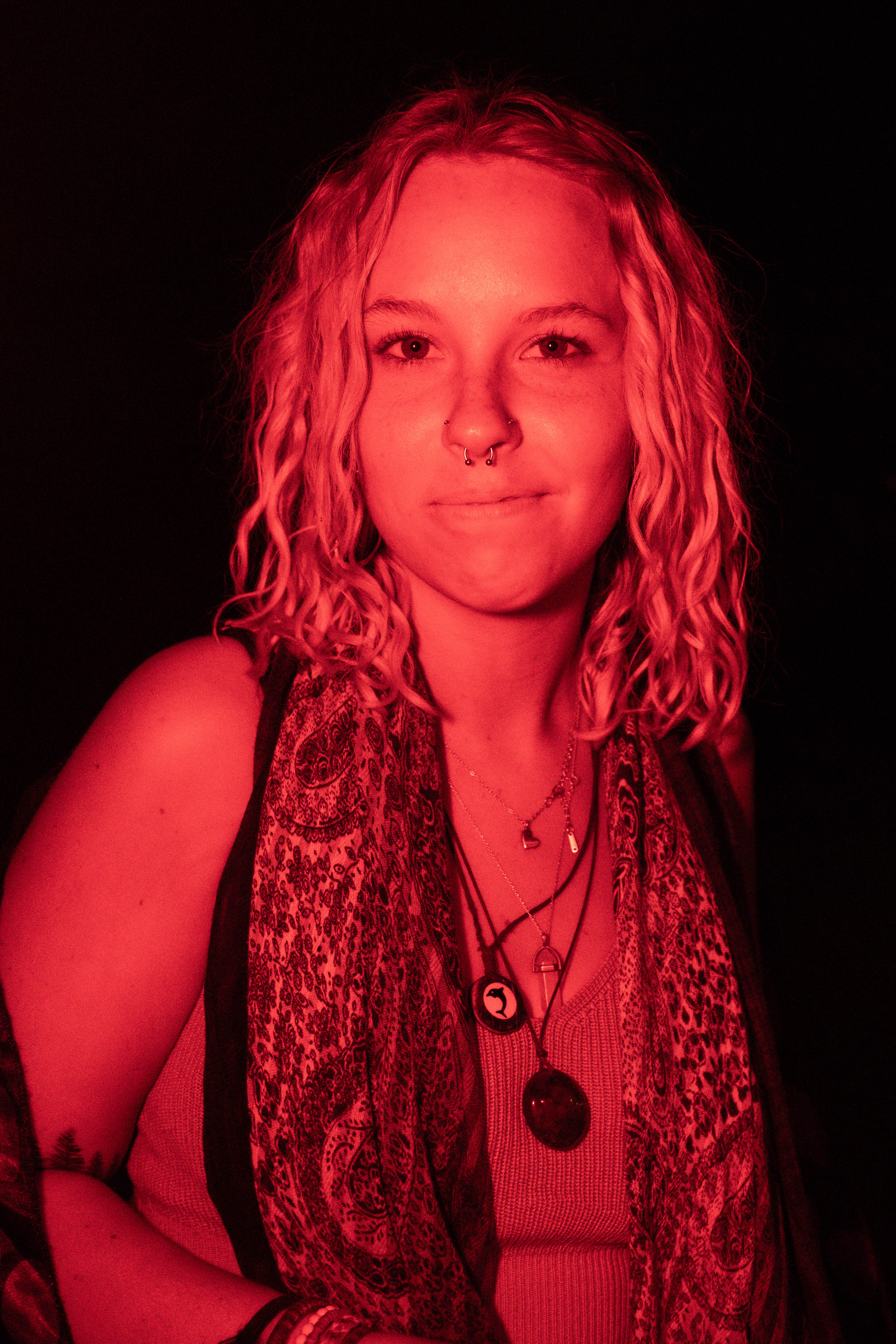 A woman wearing layered necklaces posed against a dark background in red light