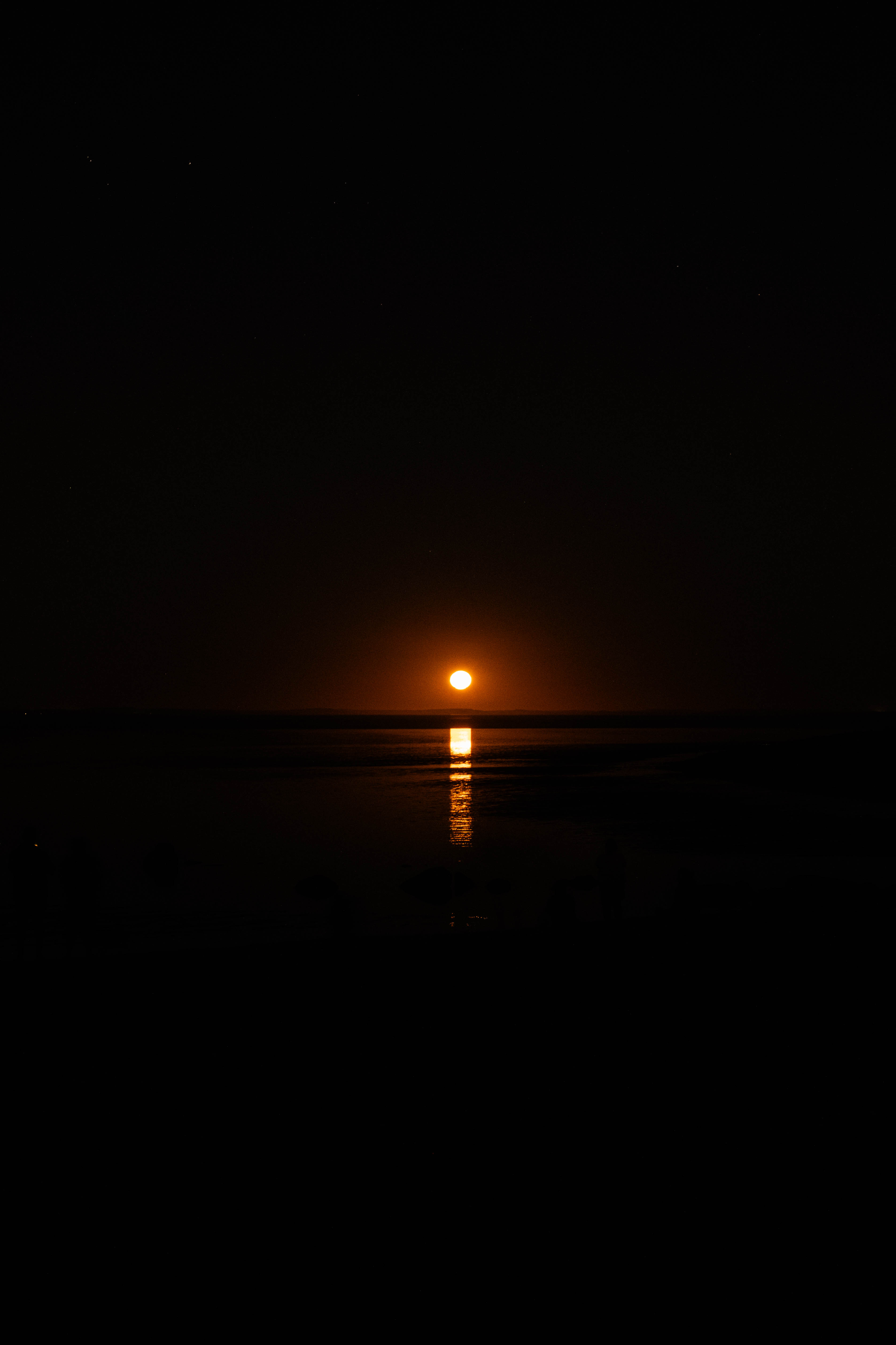 An orange moon rising over dark water with a bright reflection