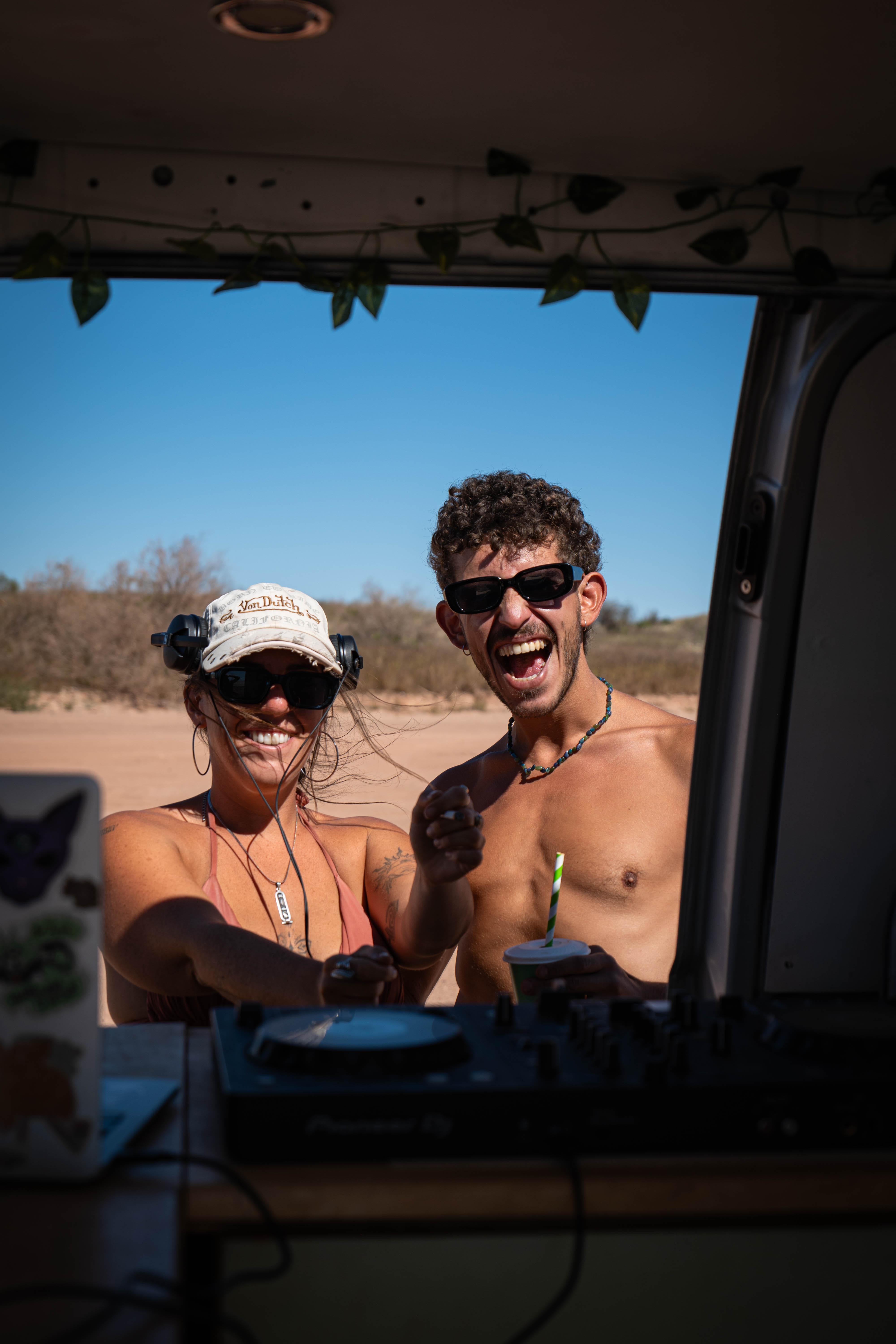 Two friends in sunglasses laughing through the open door of a campervan